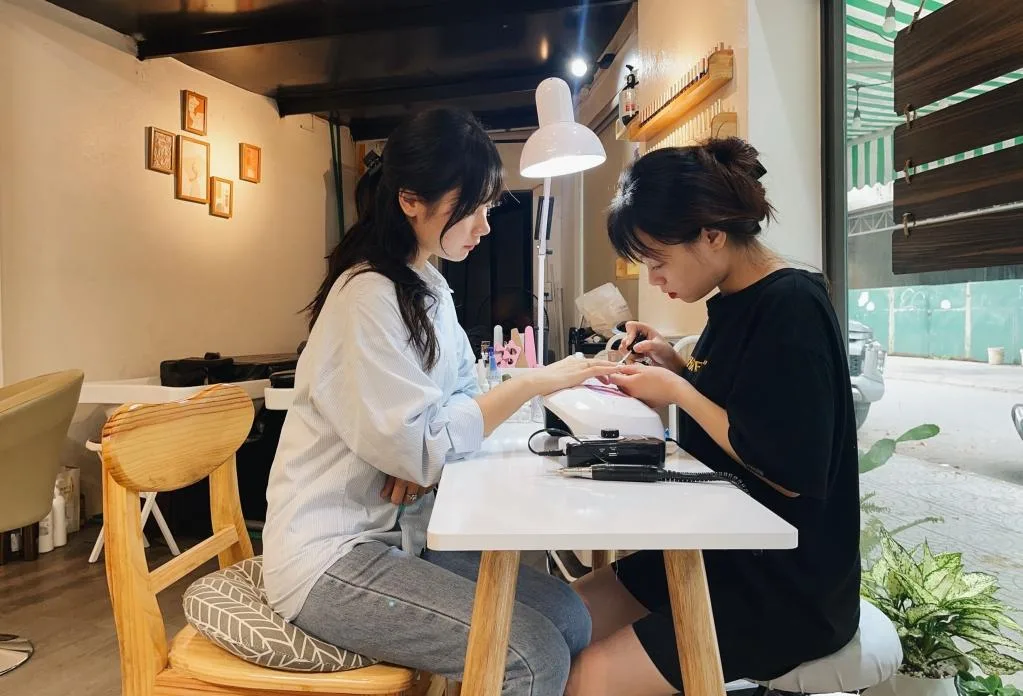 Nail technician giving a client a manicure at a salon table